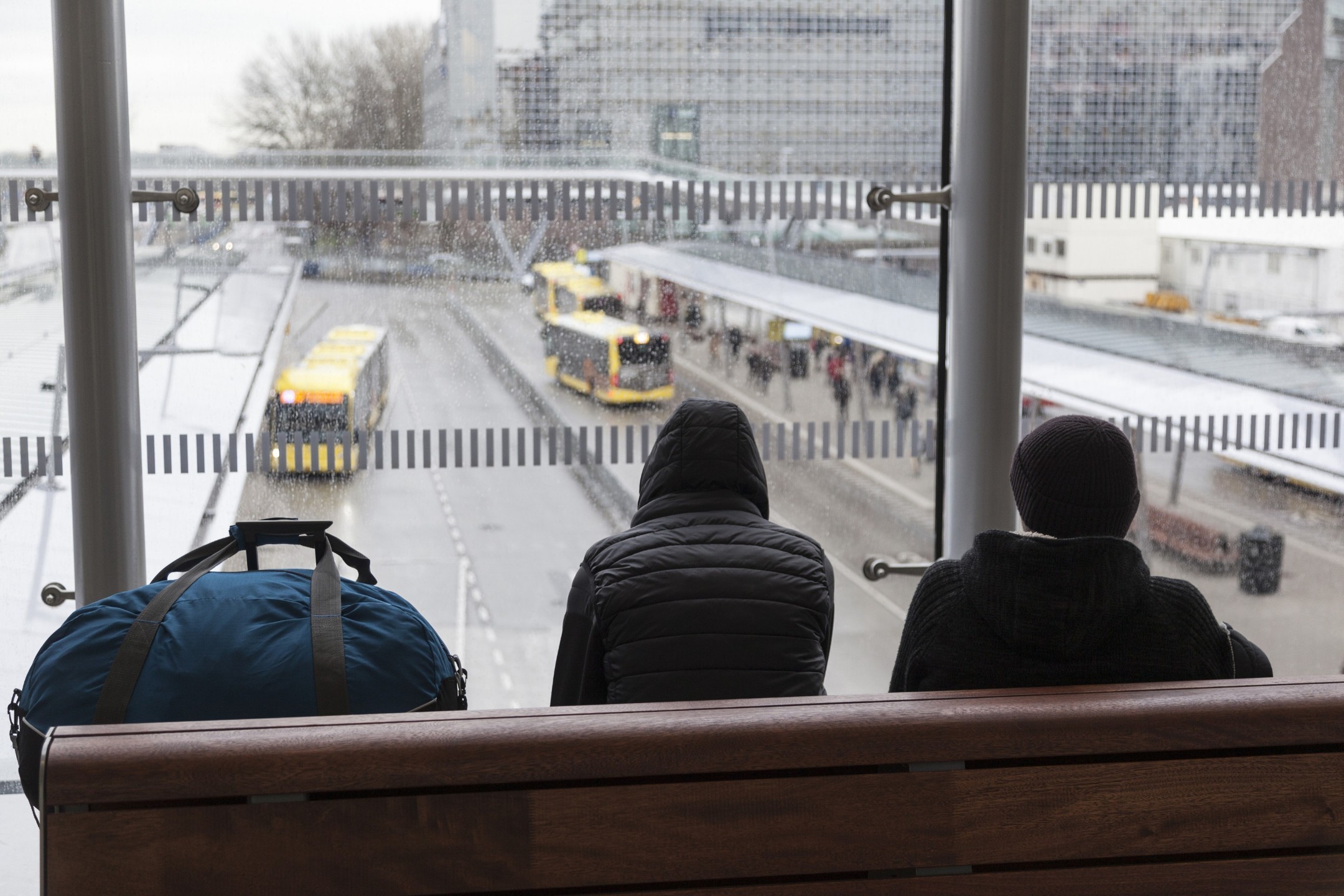 Passengers sit on a bench overlooking a bus terminal.