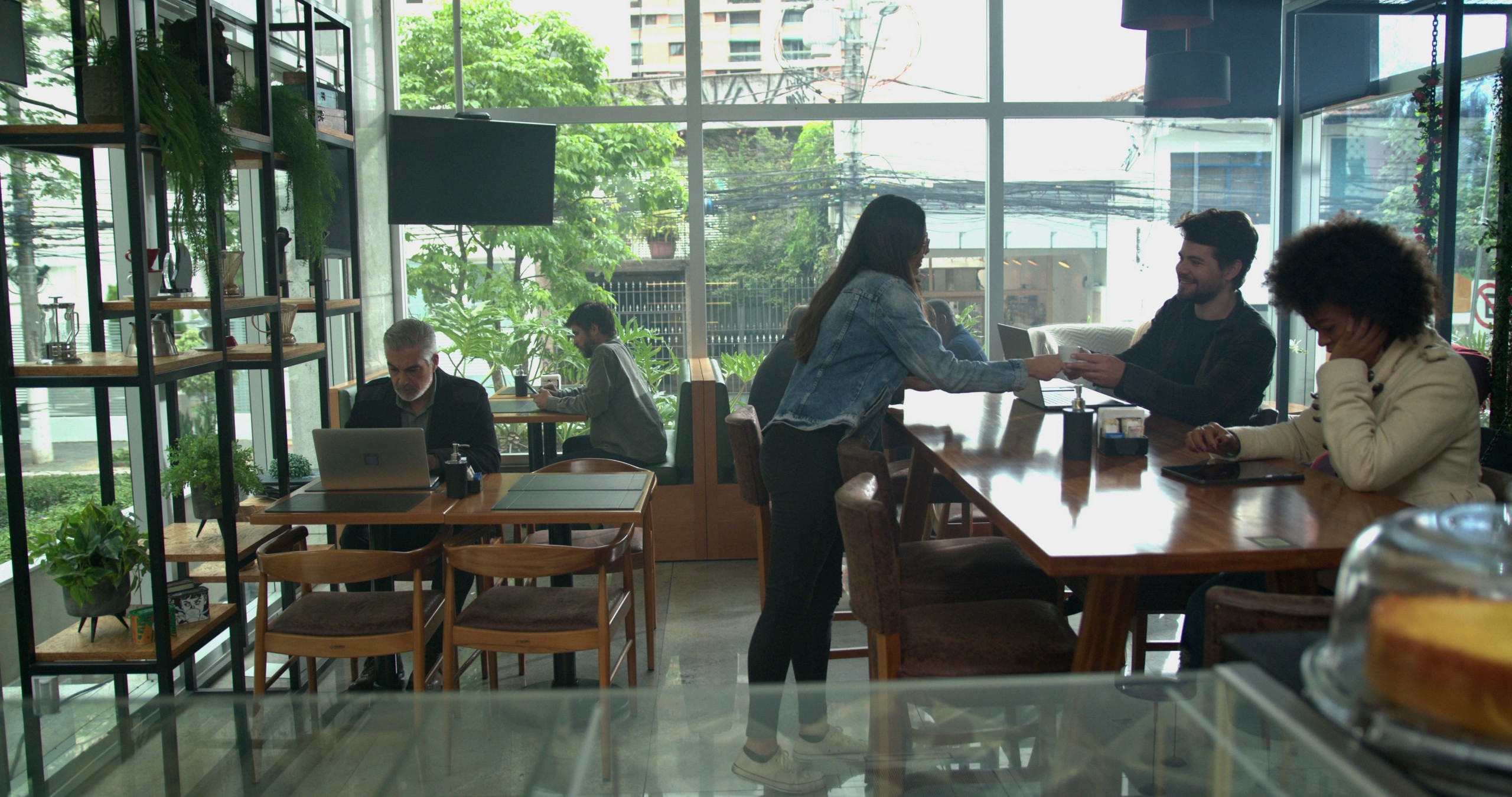 The interior of a modern cafe with lots of seating, large glass walls, and plants.