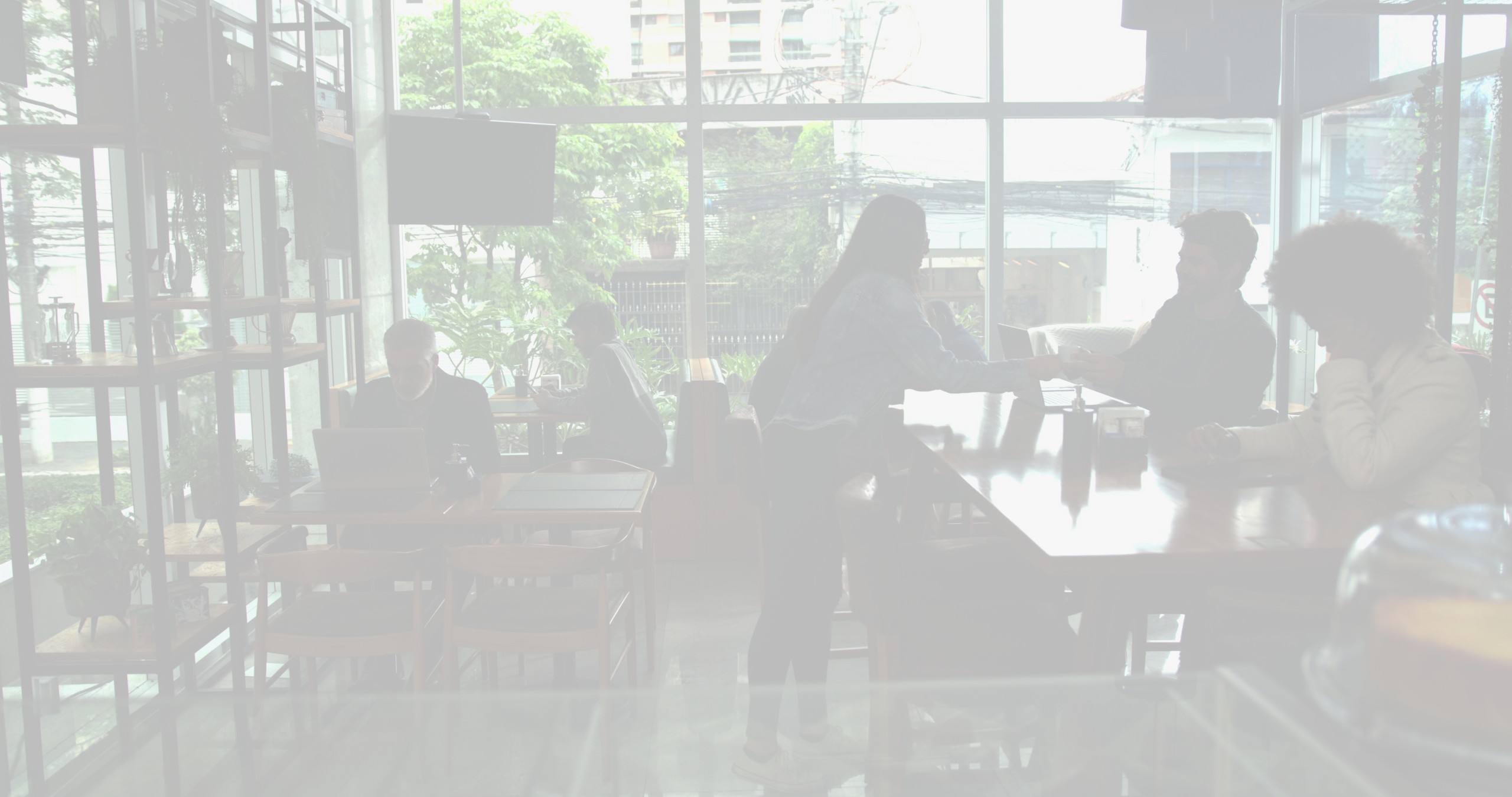 The interior of a modern cafe with lots of seating, large glass walls, and plants.