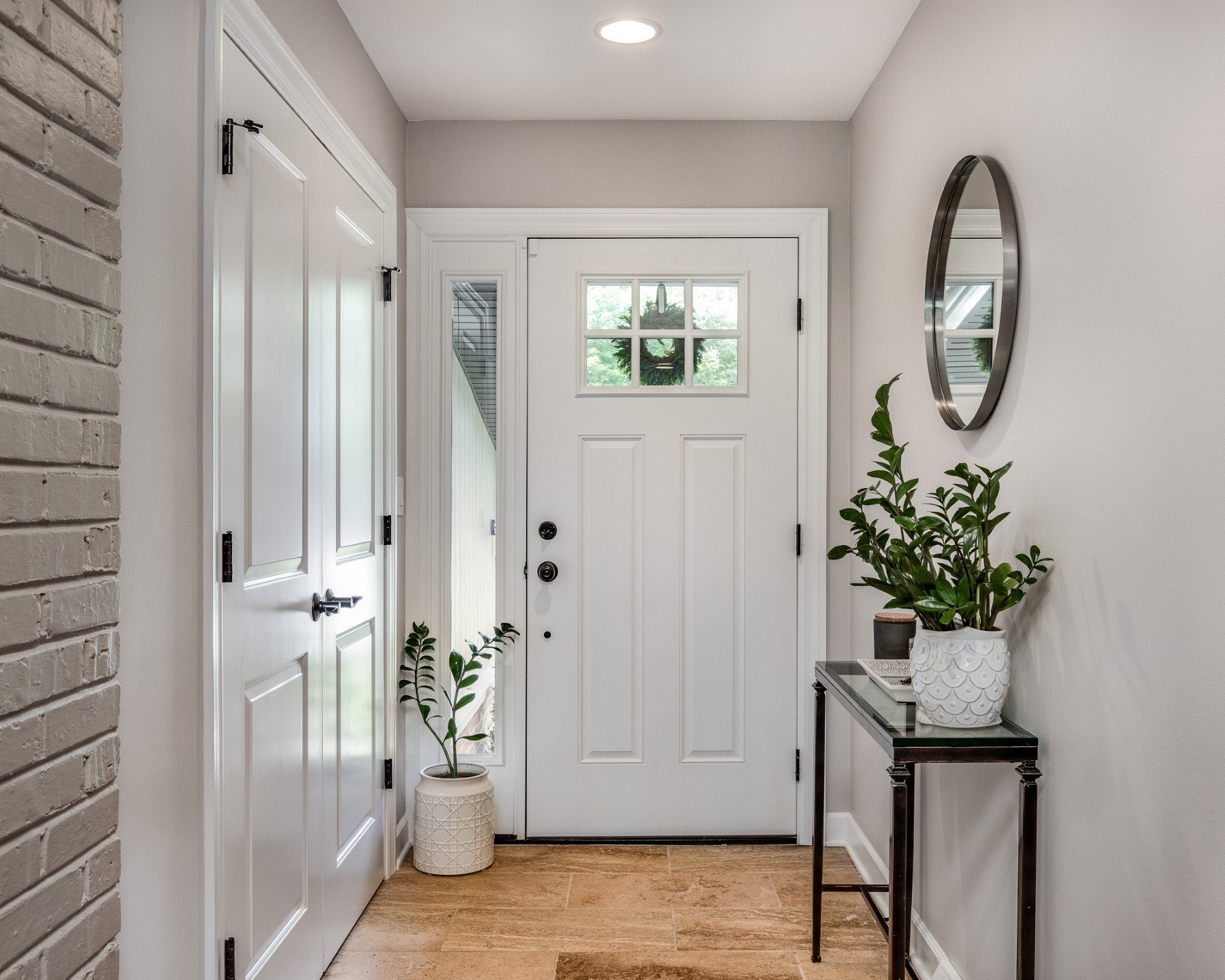 A modern front entryway of a house with a console table and plants. The front door is closed.